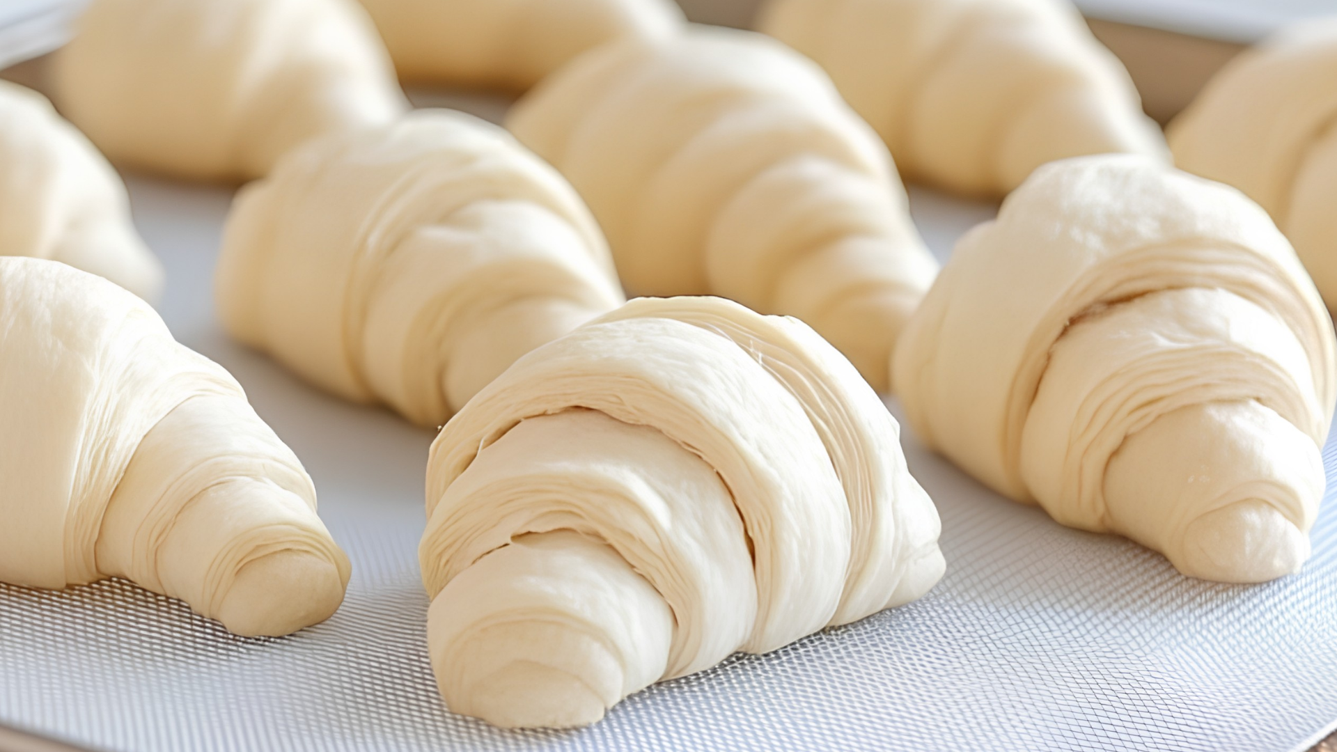 Unbaked crescent roll dough pastries arranged on a white silicone baking mat.