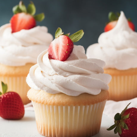 Three frosted cupcakes with whipped cream and fresh strawberry slices, arranged on a light surface with whole strawberries around them against a dark blue background.